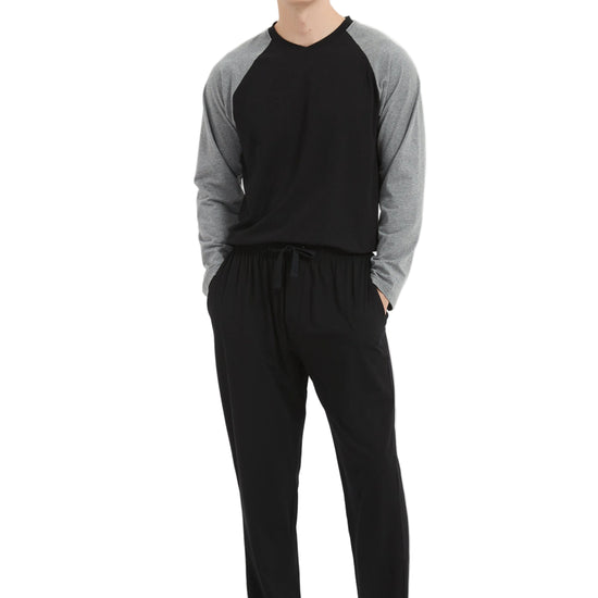 A man modeling a two-piece loungewear set consisting of a black and gray raglan long-sleeve shirt and black drawstring sweatpants, standing against a plain white studio background.