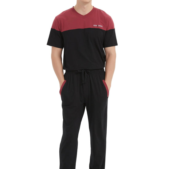A man modeling a two-piece sleepwear set consisting of a short-sleeve V-neck shirt and matching drawstring pants. The shirt features a maroon upper chest and shoulders with black sleeves and body, while the pants are solid black with side pockets.