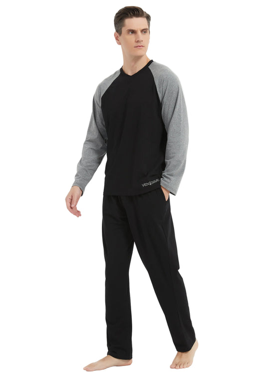 A man modeling a two-piece pajama set consisting of a black and gray raglan long-sleeve shirt and black pants, standing against a plain white studio background.