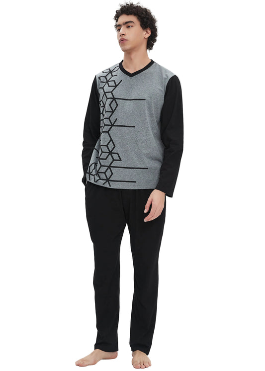 A man modeling a two-piece knit pajama set against a plain white studio background. The set includes a gray and black long-sleeve V-neck sweater vest with a geometric pattern, paired with solid black pants.