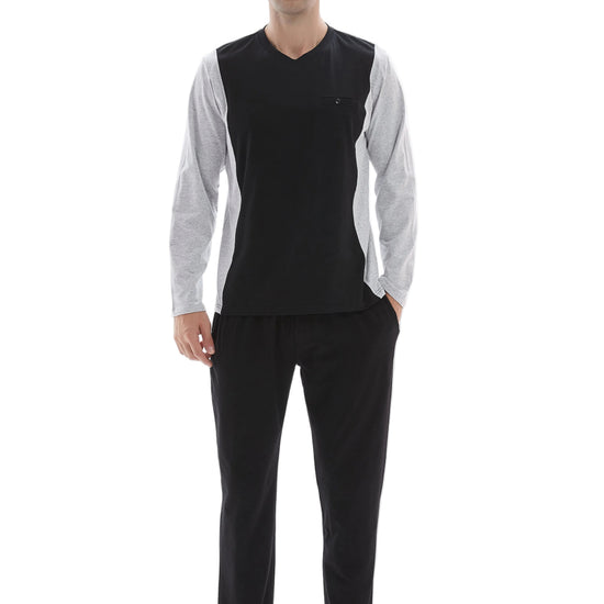 A man modeling a two-piece pajama set consisting of a black V-neck long-sleeve top with light gray sleeves and black pants, standing against a white studio background.
