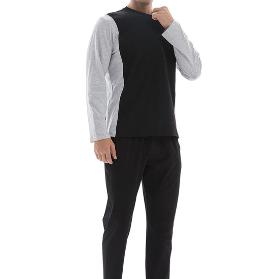 A man modeling a two-piece loungewear set consisting of a black sleeveless top over a light gray long-sleeve shirt and black pants, shot against a plain white studio background.